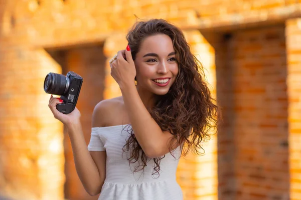 Young attractive female student or tourist using a mirrorless camera while walking in summer city. Woman takes pictures and enjoy weather. — Stock Photo, Image