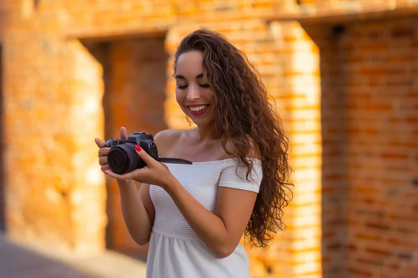 Joven atractiva estudiante o turista usando una cámara sin espejo mientras camina en la ciudad de verano. Mujer toma fotos y disfruta del clima. — Foto de Stock