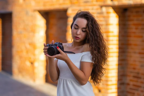 Jonge aantrekkelijke vrouwelijke student of toerist met behulp van een spiegelloze camera tijdens het wandelen in de zomerstad. Vrouw neemt foto 's en geniet van het weer. — Stockfoto