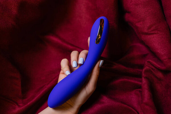 Женщина в спальне держит вибратор в руке.