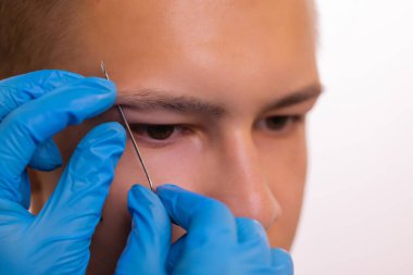 Kaşlı adam. Üç küçük siyah piercing.