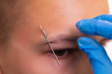 Kaşlı adam. Üç küçük siyah piercing.