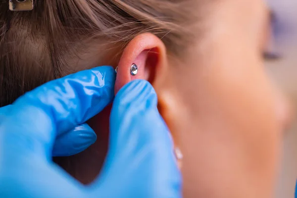 Profissional segurando a jóia de piercing pouco antes de parafusar a bola. — Fotografia de Stock