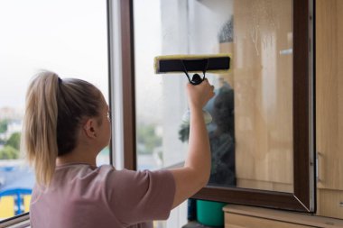 İş kıyafetleri içinde, evdeki profesyonel aletlerle pencereleri yıkayan güzel bir ev hanımı..