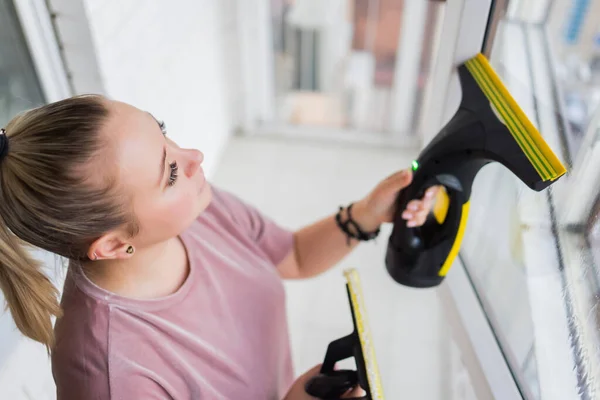 Красива молода домогосподарка в робочому одязі миє вікна професійними інструментами вдома . — стокове фото