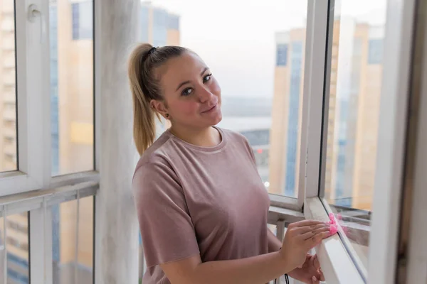 Hermosa joven ama de casa en la ropa de trabajo lavando ventanas por herramientas profesionales en casa. — Foto de Stock