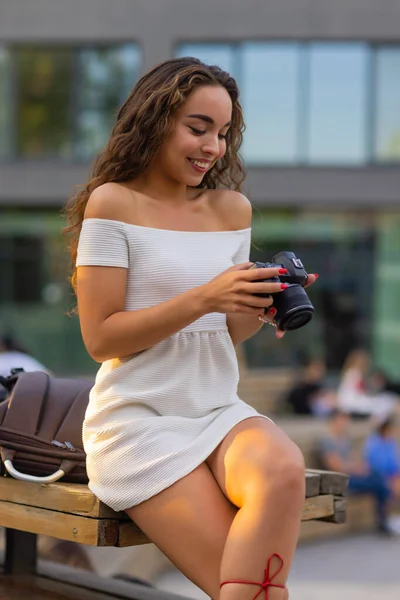 Mladá atraktivní studentka nebo turistka používající bezzrcadlovou kameru při procházce v letním městě. Žena fotí a užívá si počasí. — Stock fotografie