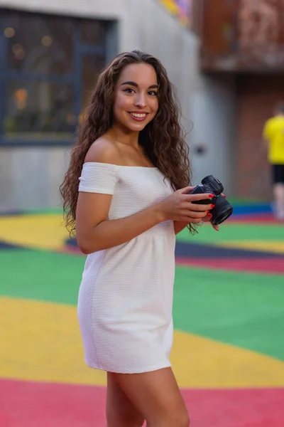 Jonge aantrekkelijke vrouwelijke student of toerist met behulp van een spiegelloze camera tijdens het wandelen in de zomerstad. Vrouw neemt foto 's en geniet van het weer. — Stockfoto