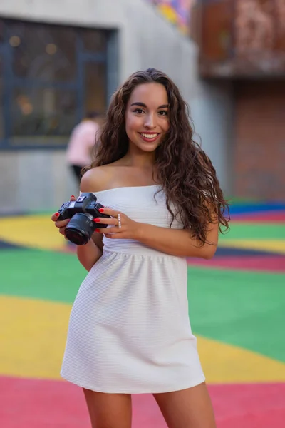 Jonge aantrekkelijke vrouwelijke student of toerist met behulp van een spiegelloze camera tijdens het wandelen in de zomerstad. Vrouw neemt foto 's en geniet van het weer. — Stockfoto