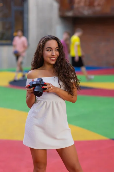 Jonge aantrekkelijke vrouwelijke student of toerist met behulp van een spiegelloze camera tijdens het wandelen in de zomerstad. Vrouw neemt foto 's en geniet van het weer. — Stockfoto