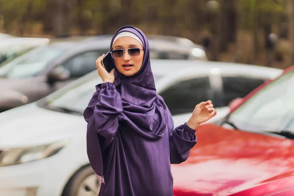 Islamitische prachtige vrouw in een islamitische jurk staande op een zomer park straat achtergrond bos herfst bomen.wereld hijab dag. — Stockfoto