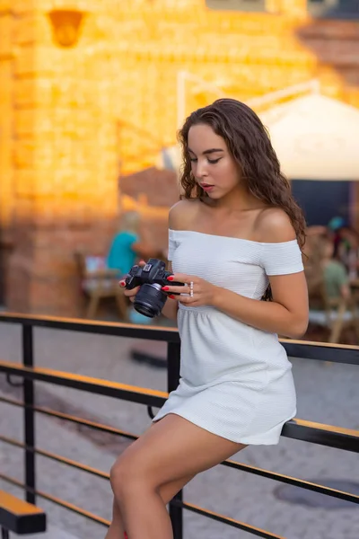 Молода приваблива студентка або туристка використовує бездзеркальну камеру під час прогулянки в літньому місті. Жінка фотографує і насолоджується погодою . — стокове фото