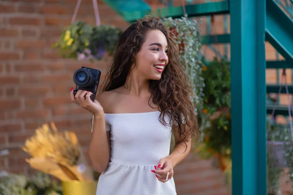 Jonge aantrekkelijke vrouwelijke student of toerist met behulp van een spiegelloze camera tijdens het wandelen in de zomerstad. Vrouw neemt foto 's en geniet van het weer. — Stockfoto