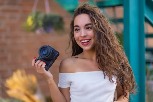 Jonge aantrekkelijke vrouwelijke student of toerist met behulp van een spiegelloze camera tijdens het wandelen in de zomerstad. Vrouw neemt foto 's en geniet van het weer. — Stockfoto