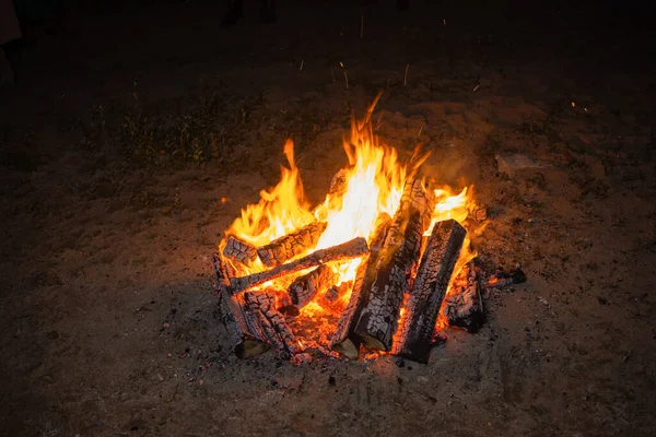 Fénykép egy éjszakai tábortűzről sötét háttérrel. A lángok szikrákat szórnak szét minden irányba. Fényesen égő narancsszínű tűz. — Stock Fotó