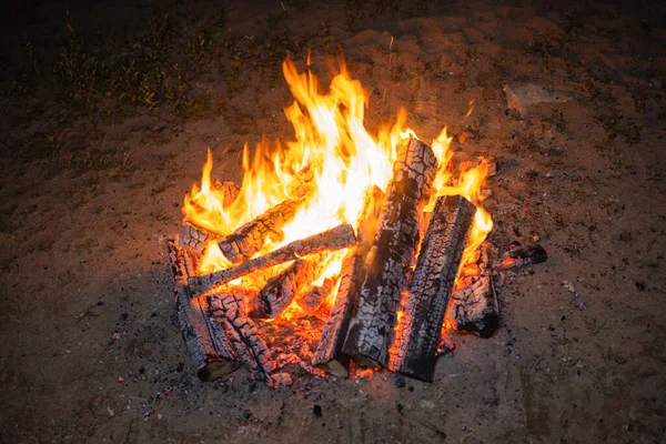 Foto de una hoguera nocturna sobre un fondo oscuro. Las llamas dispersan chispas en todas direcciones. Fuego naranja brillantemente ardiendo. — Foto de Stock