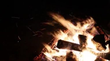 Karanlık bir arka plana karşı şenlik ateşi. Alevler her yöne kıvılcımlar saçar. Parlak turuncu ateş.