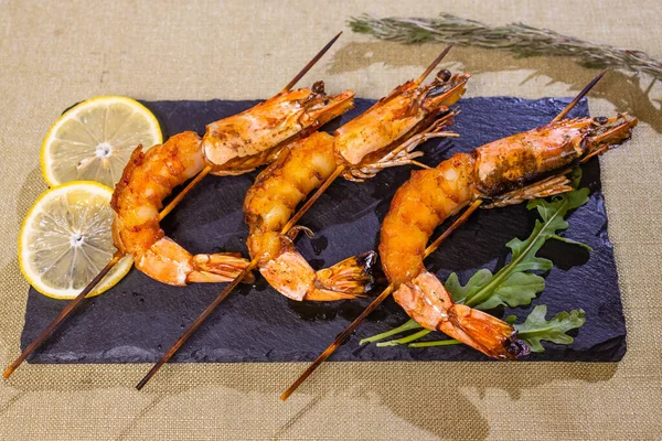 Frutos do mar. Marisco. Camarão grelhado frito em espetos de madeira, copo de vinho branco. Lanche, aperitivo. Em mesa de concreto preto, vista superior. — Fotografia de Stock