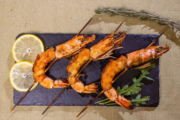 Frutos do mar. Marisco. Camarão grelhado frito em espetos de madeira, copo de vinho branco. Lanche, aperitivo. Em mesa de concreto preto, vista superior. — Fotografia de Stock