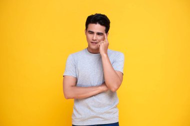 Yakışıklı Asyalı dalgın adam sarı arka planda soyutlanmış düşünüyor..