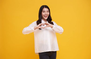 Sarı arka planda kalp işareti gösteren güzel bir Asyalı kadın. Aşk ve mutlu sevgililer günü konsepti.