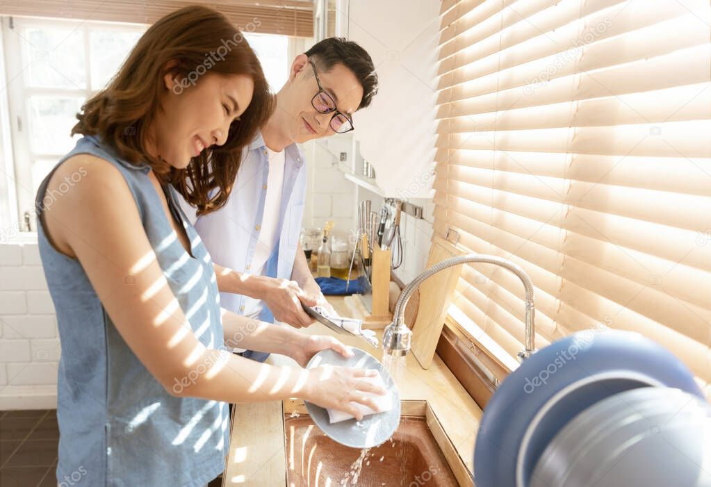 Happy Asian couple family washing dishes together at kitchen after breakfast.