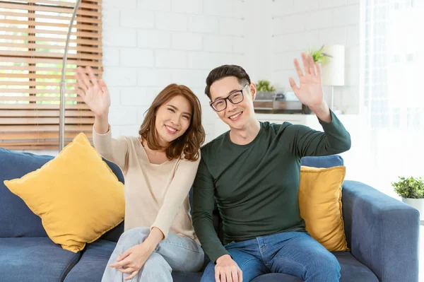 Happy Asian couple man and woman video call virtual meeting together on sofa at home living room.