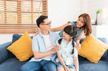 Mutlu Asyalı aile, oturma odasındaki kanepede kucaklaşıyor..