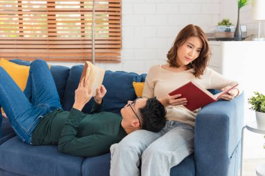 Mutlu Asyalı çift hafta sonunu evde kanepede oturup kitap okuyarak geçiriyorlar..