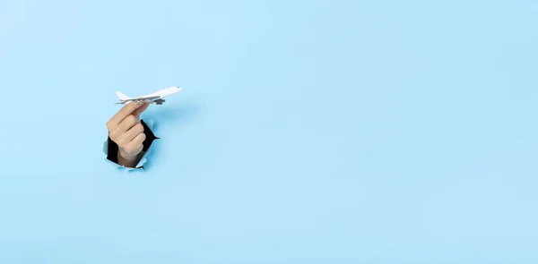 Business Hand holds model plane from a hole in the wall on blue background.  insurance travel concept. Panoramic image