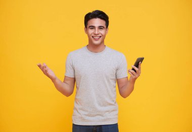 Sarı arka planda cep telefonuyla kutlama yapan yakışıklı Asyalı adam..