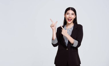 Happy Confident Asian business woman pointing finger on blank space beside isolated on gray background.	