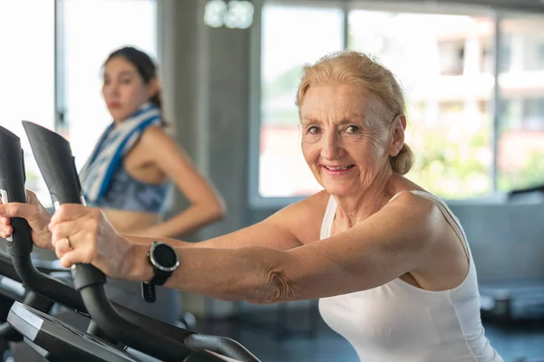 Senior woman exercising spinning bike in fitness gym. elderly healthy lifestyle concept.