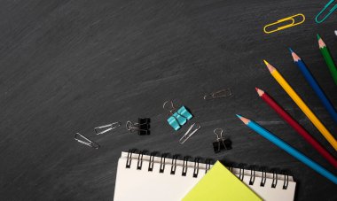 Okula geri dön. Kara tahta arka planında aksesuarlar, kitaplar ve pastel boyalar. en üstteki görünüm.