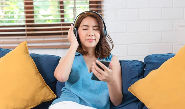 Молода Азіатка Використовує Смартфон Слухає Музику Підключившись Навушників Сидячи Дивані — стокове фото