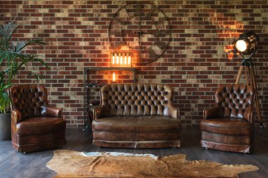 Oturma odasında pahalı bir dekor. Deri koltuk ve sandalyeler tuğla duvara dayanıyor.