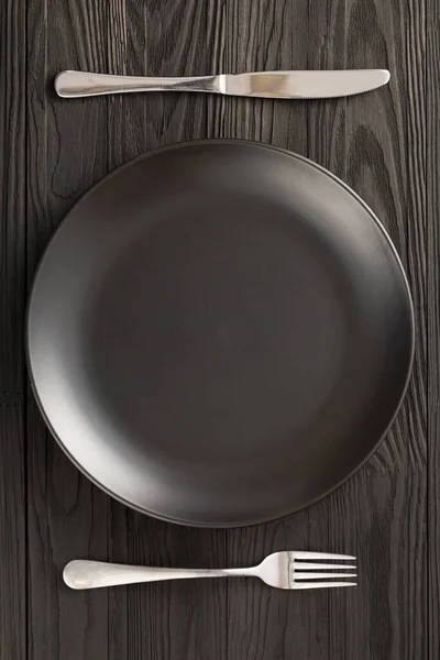 Κενό μαύρο πιάτο σερβίρει ξύλινο τραπέζι, πάνω όψη — Φωτογραφία Αρχείου