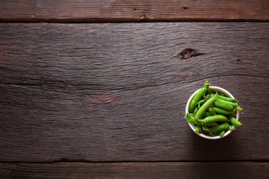 Tahta bir masanın üzerindeki kabın içinde yeşil bezelye kabukları ve fotokopi alanı