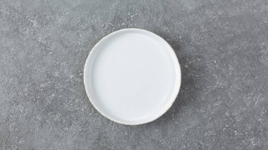 Gri beton arka planda boş beyaz plaka. Boşluğu kopyala, üst görünüm.