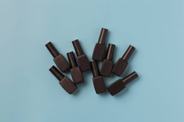 Mavi arka planda siyah manikür şişeleri bulunan minimal bileşim.