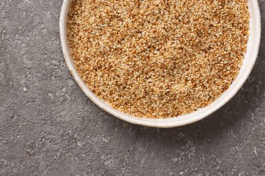 Gri beton arka planda bir kasede susam tohumları.