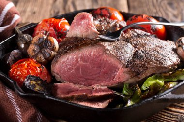 Sebzelerle dolu dökme demir bir tavada kızartılmış bir et parçası, yakın plan.