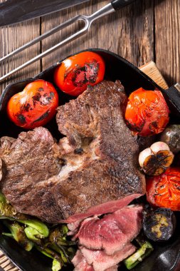 Sebzelerle dolu dökme demir bir tavada kızartılmış bir et parçası, yakın plan.