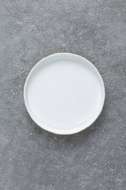 Gri beton arka planda boş beyaz plaka. Boşluğu kopyala, üst görünüm.