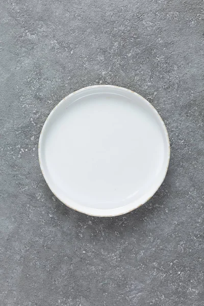 Gri beton arka planda boş beyaz plaka. Boşluğu kopyala, üst görünüm.