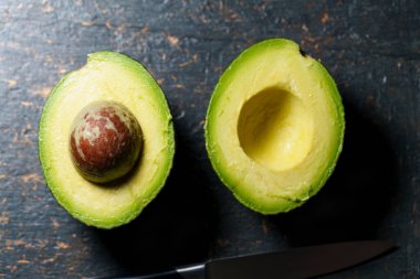 Olgun avokado koyu renkli bir taş yüzeyde ikiye bölünmüş..