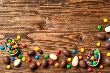 Kırsal ahşap masa üzerinde renkli Paskalya tatlıları, kopya alanı olan şenlikli bahar afişi.