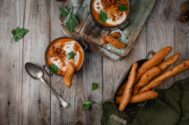 Lezzetli kavrulmuş biber çorbası, çıtır nohut ve krema tencerede, ekmek ve kaşıkla ahşap masada.