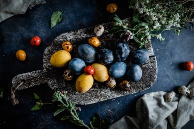 Ahşap kesim tahtası, dekoratif boyalı Paskalya yumurtaları ve kırsal ahşap arka planda taze çiçekler, yakın görüş.