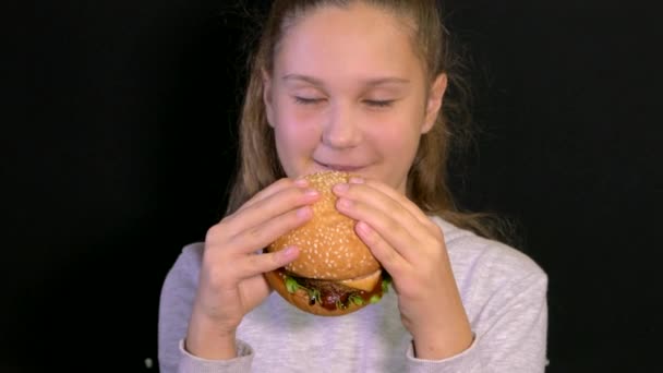 Une jeune fille mange un délicieux hamburger. Restauration rapide snack. Tenez la nourriture en main — Video